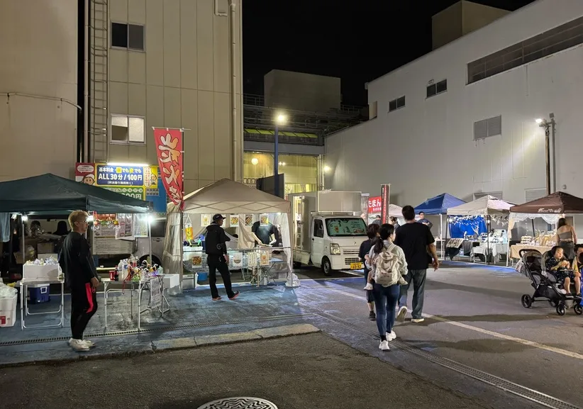 夜の駐車場に屋台とキッチンカーが並び、来場者が通りを歩いている様子。