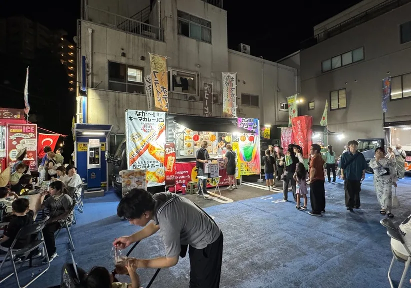 夜の駐車場に設けた飲食スペースで、来場者が椅子に座って食事をしている様子。