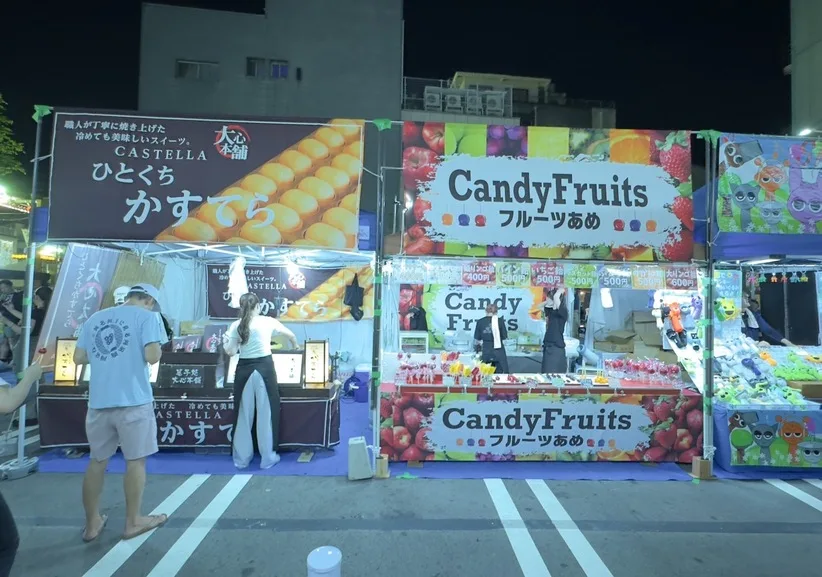 横並びに設営された菓子・フルーツあめ・くじ引きの出店を正面から見た様子。